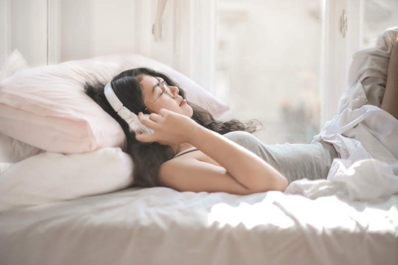 woman lying on bed while listening to music | fighting stress