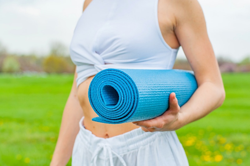 woman standing and holding blue yoga mat | stress reducers