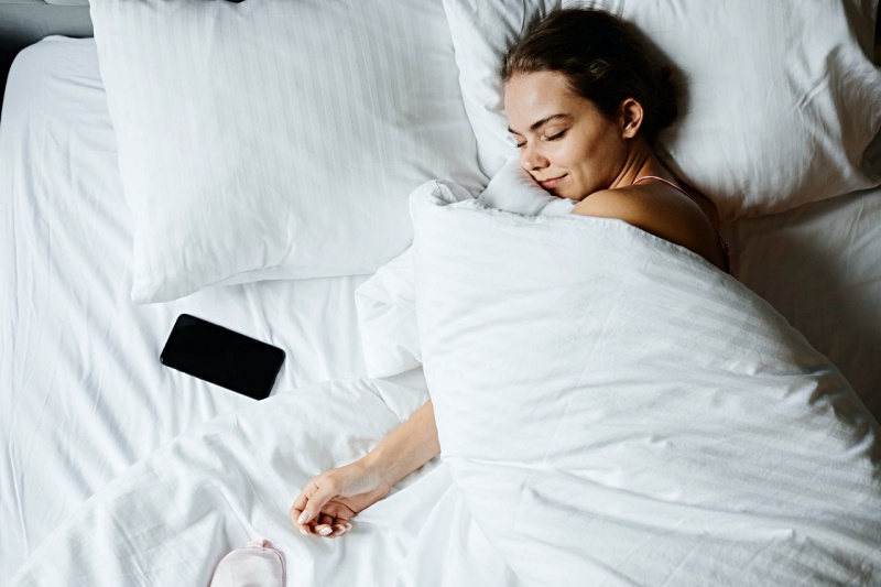 a woman sleeping beside her smartphone | how to improve sleep quality