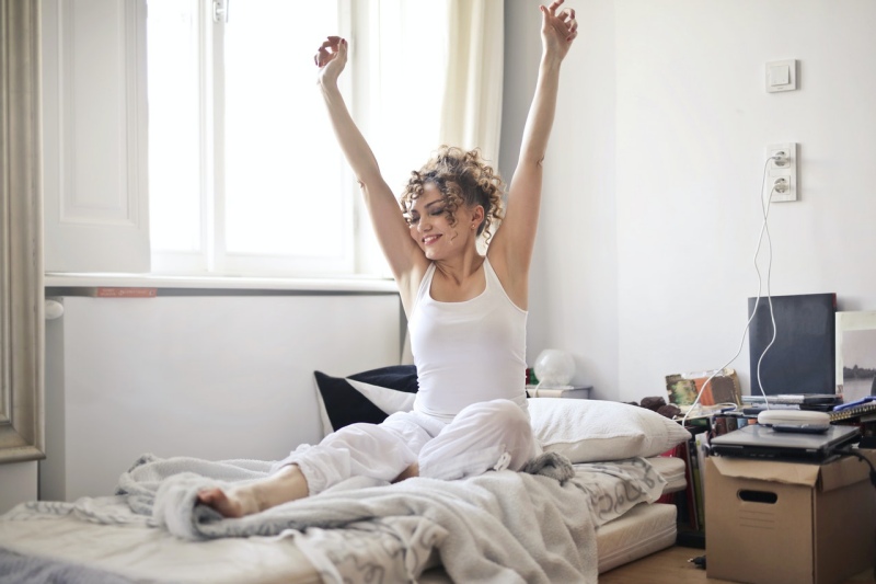photo of woman in white vest and pants sitting on a mattress while stretching her hands | memory foam mattress