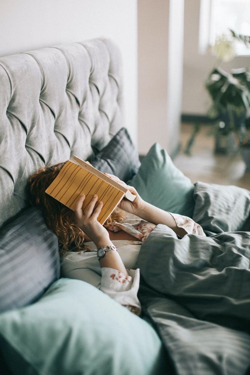 woman covering face with book on bed | adjustable bed base