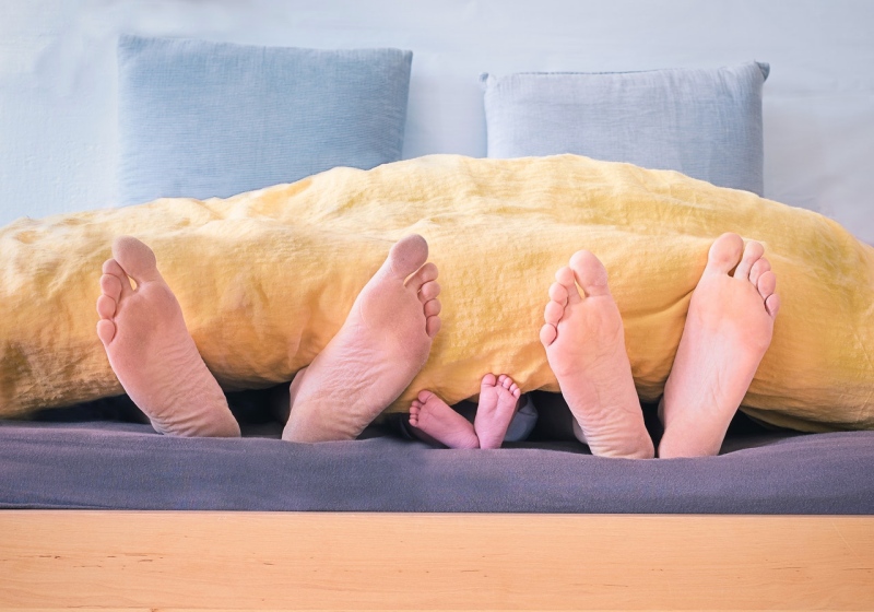 family of three lying on bed showing feet while covered with yellow blanket | mattresses