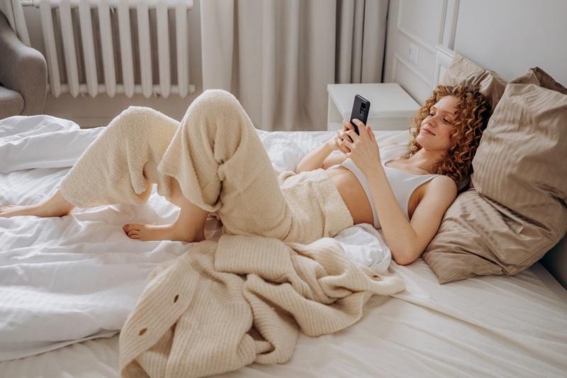 woman in white crop top lying down on bed using smartphone | hybrid mattress
