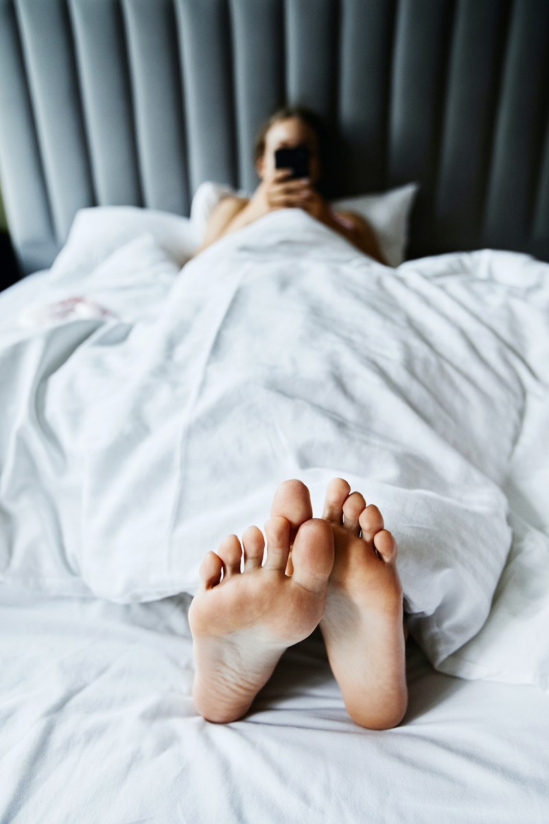 person using her smartphone while lying on the bed | sleep hygiene tips