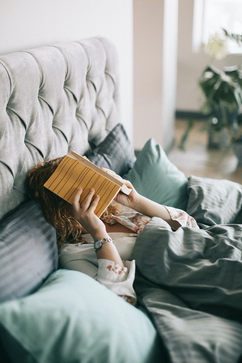 woman covering face with book on bed | sleep hygiene tips