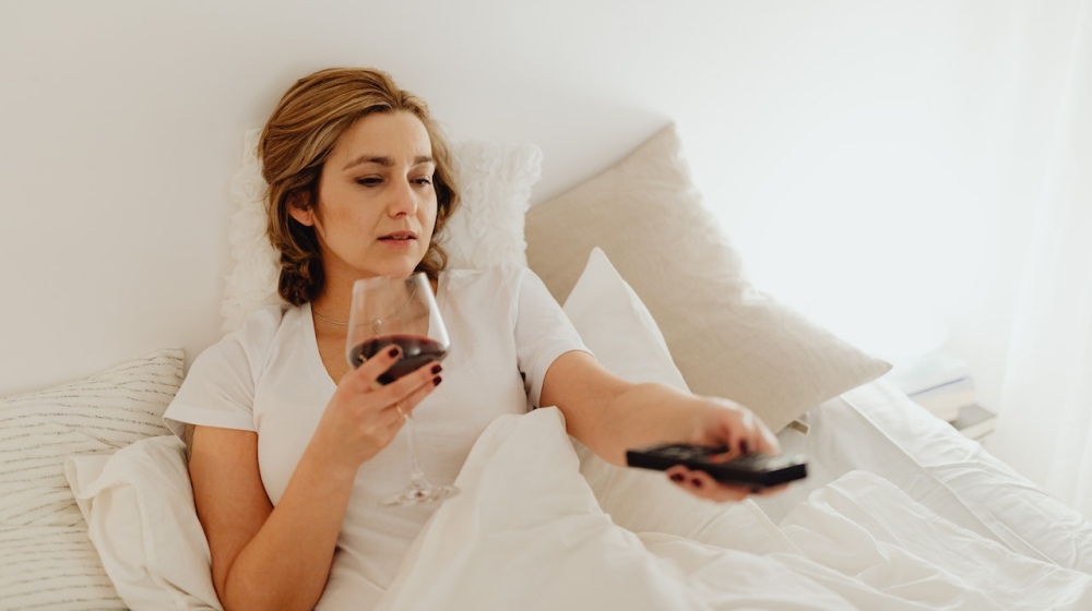 woman relaxing in bed with wine adn watching tv | What Is Revenge Bedtime Procrastination And How To Overcome It | Featured