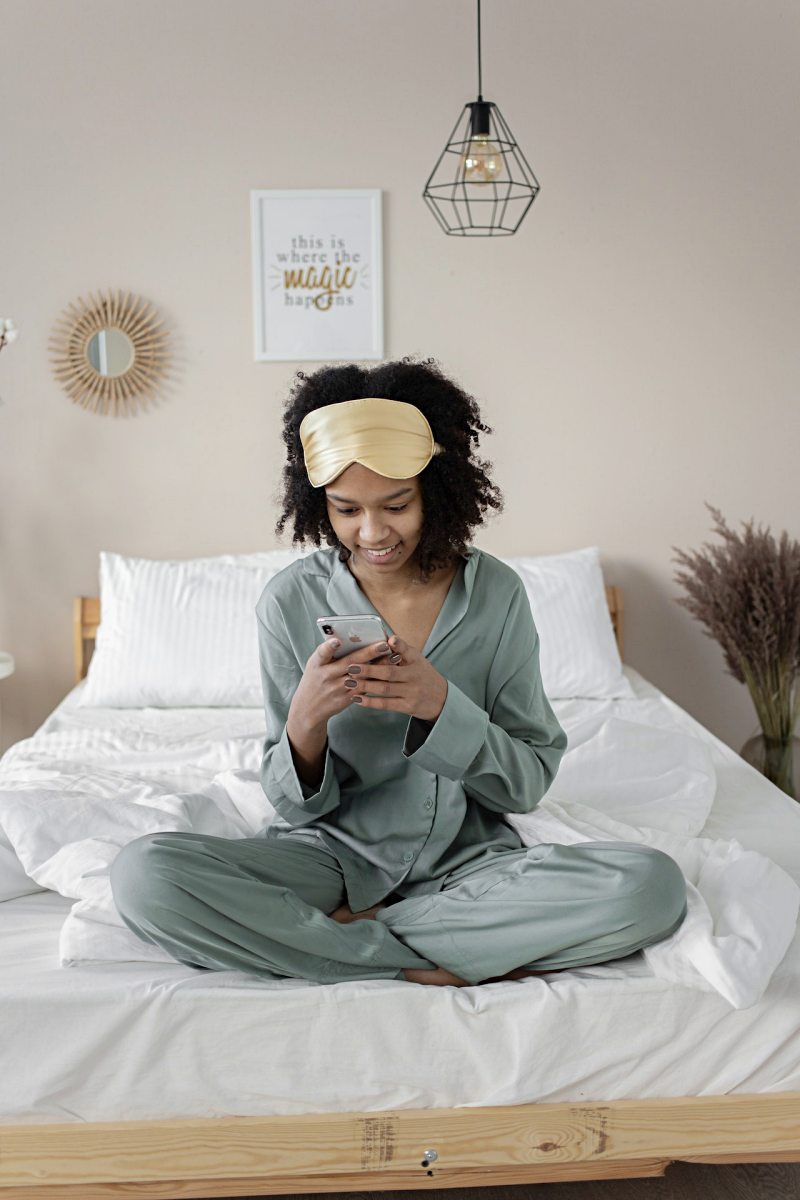 woman wearing pajama and sleeping mask using phone in bed | procrastination