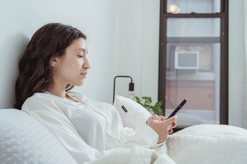 calm woman resting on bed with smartphone | poor sleep