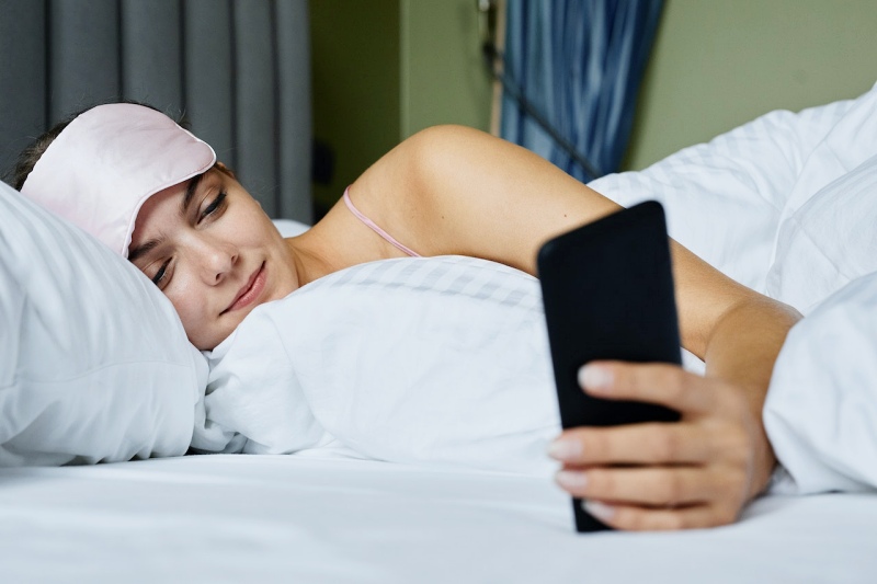 a woman using a mobile phone while lying in the bed | orthosomnia meaning