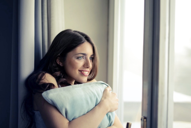 woman hugging white pillow beside glass door | best pillow for jaw clenching