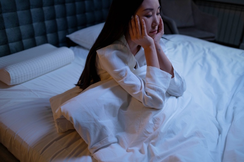 woman in white long sleeve shirt sitting on a bed | sleeplessness