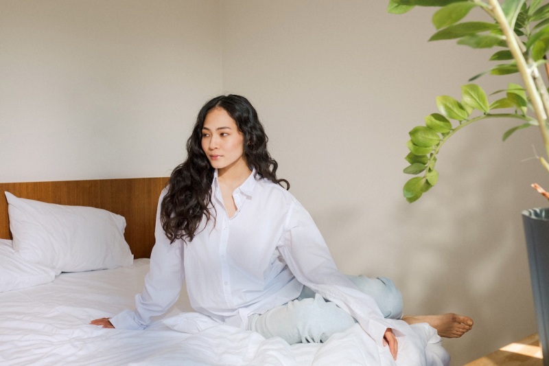 attractive woman with long curly hair sitting in bed in white pyjamas | mattress covers for allergies for dust
