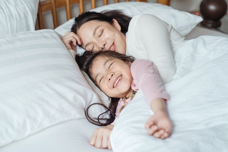 cheerful mother and daughter resting in bed | orthopedic pillow for neck