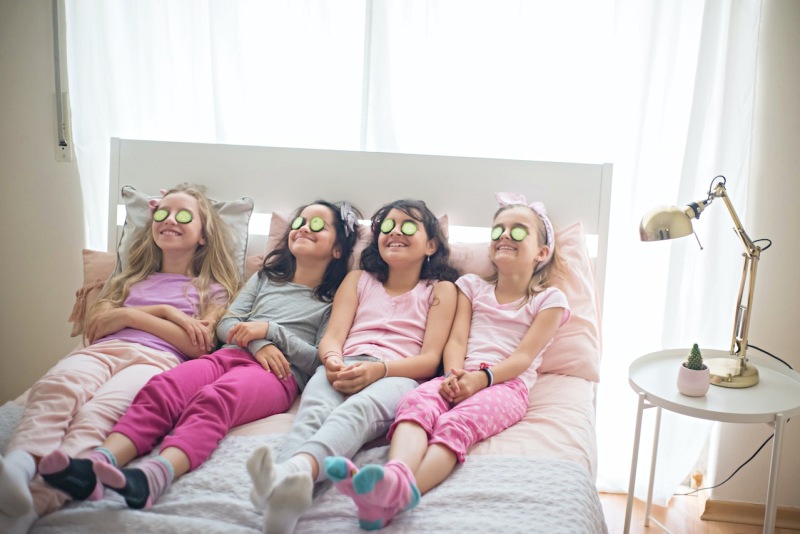 girls in pajamas with cucumbers on eyes sitting on bed | full size