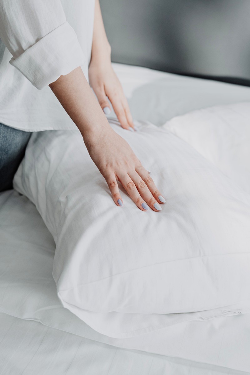 person in white shirt and gray denim jeans sitting on white bed | gel pillow