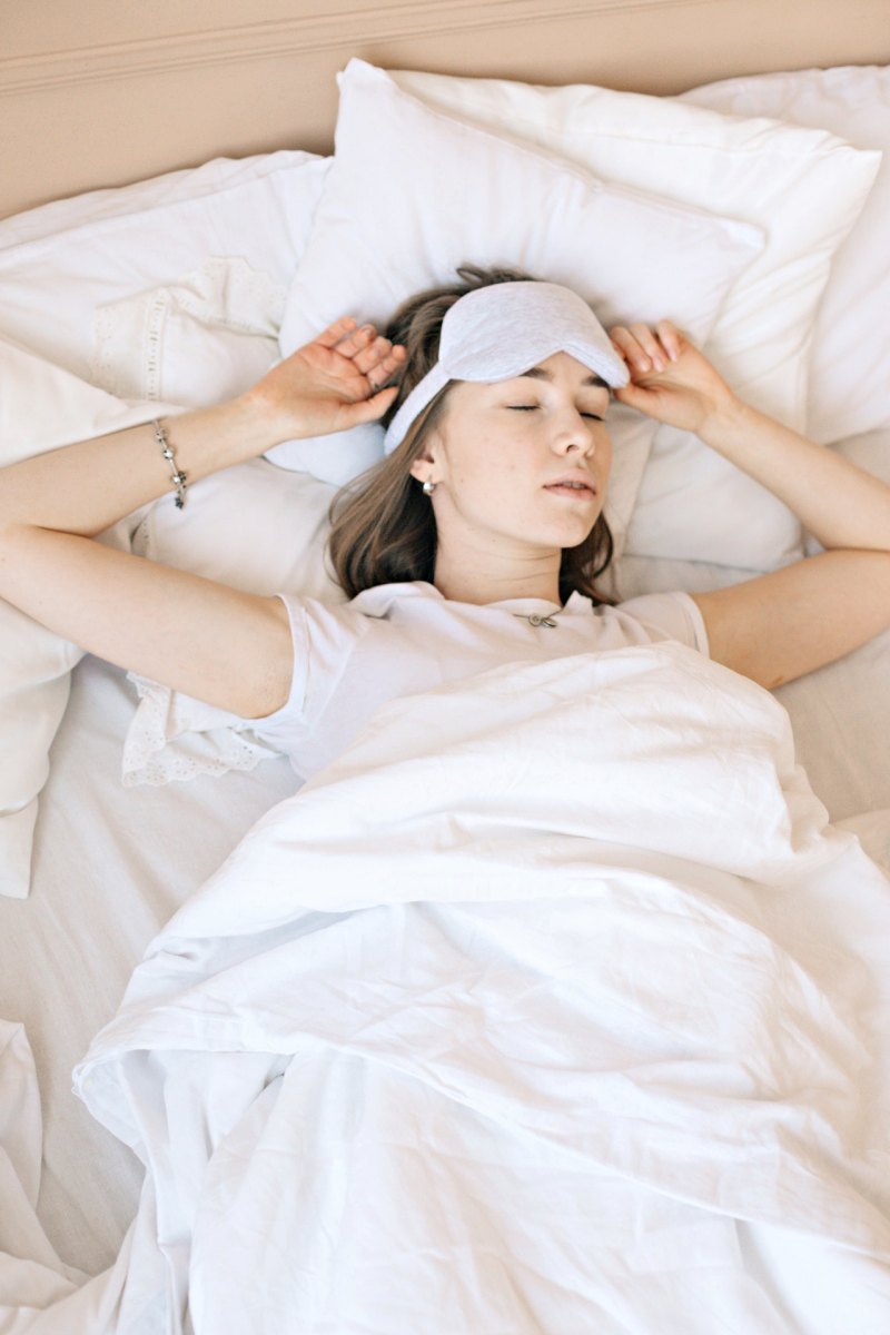 a woman lying in bed with a sleep mask | should shoulders be on pillow when sleeping
