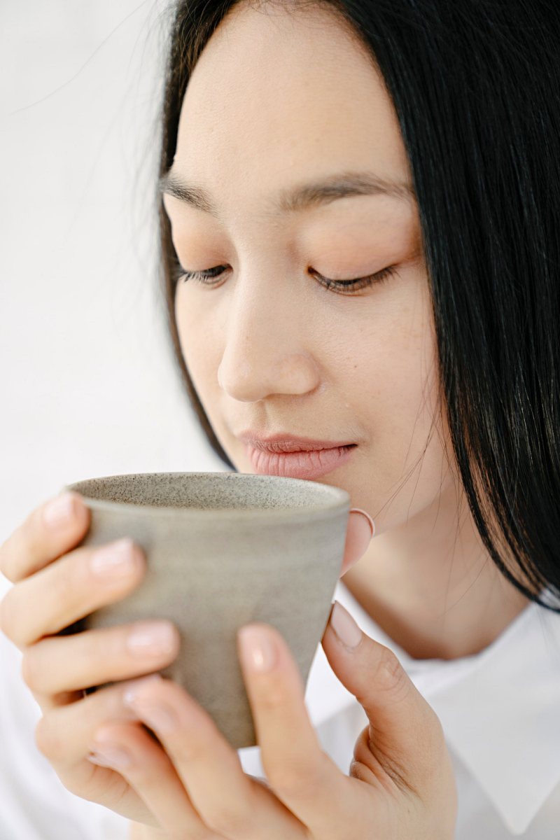 tranquil young asian lady drinking tea in white room | herbs to aid sleep