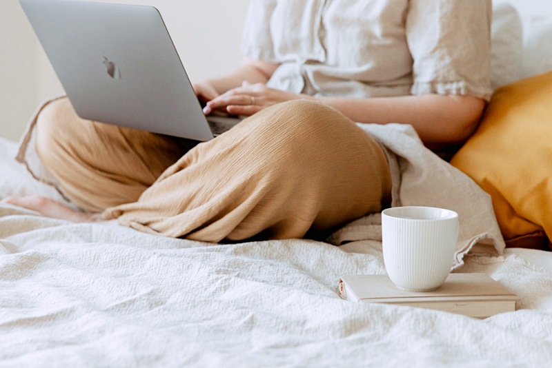 woman lounging with laptop and cup of coffee on the bed | memory foam vs innerspring