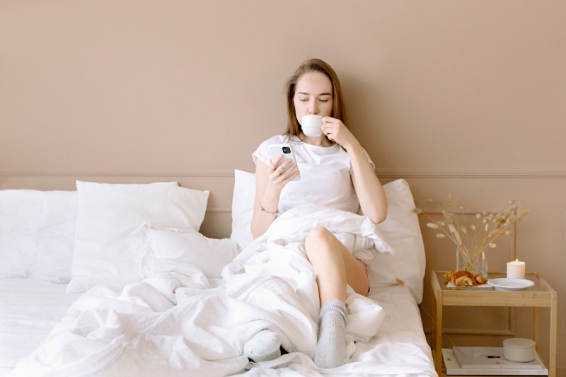 woman drinking from a mug while sitting on the bed | mattress for athletes
